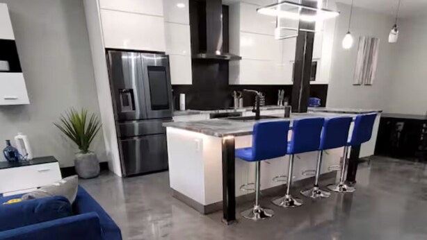 Una cocina moderna con una isla central, taburetes de bar y electrodomésticos de acero inoxidable.