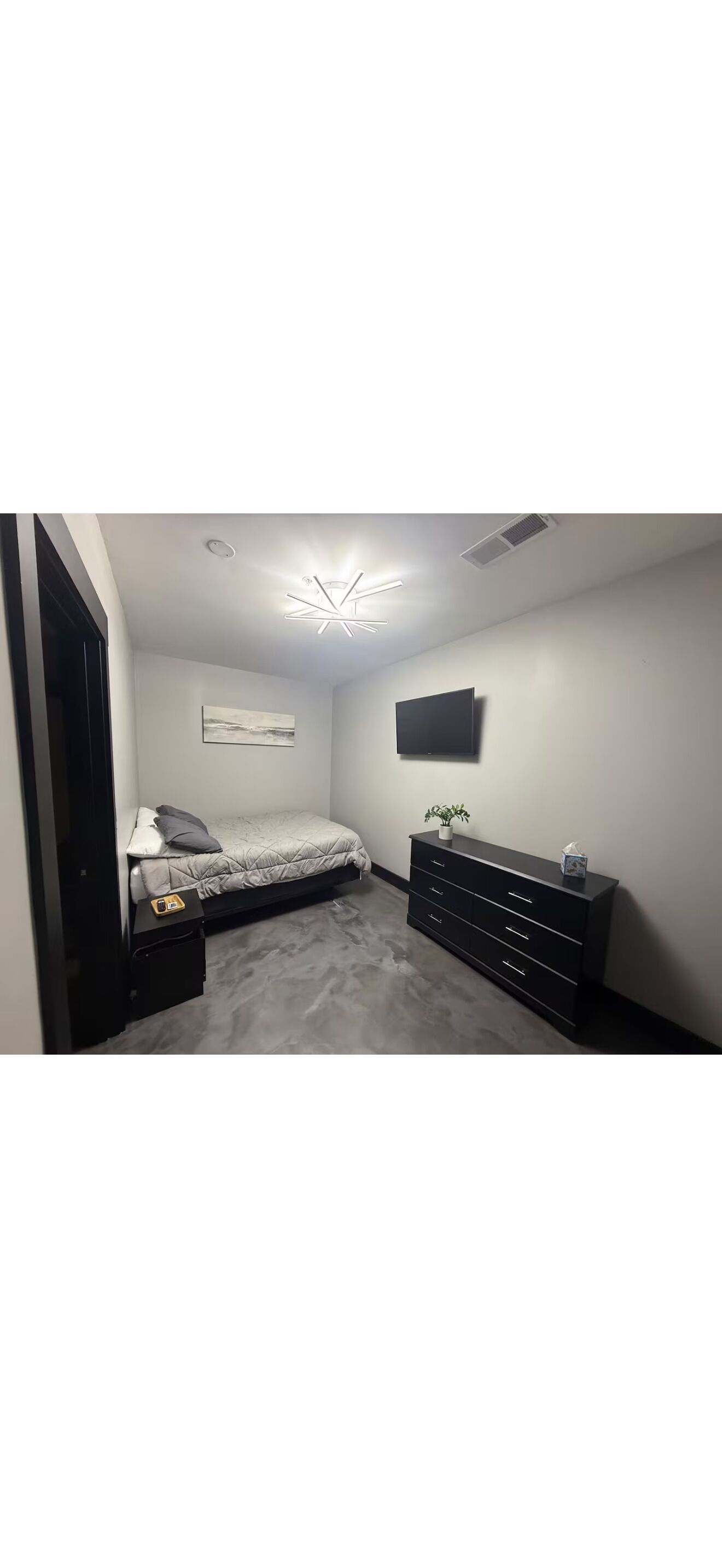 A bedroom with a bed, a dresser, a television, and a ceiling light fixture.
