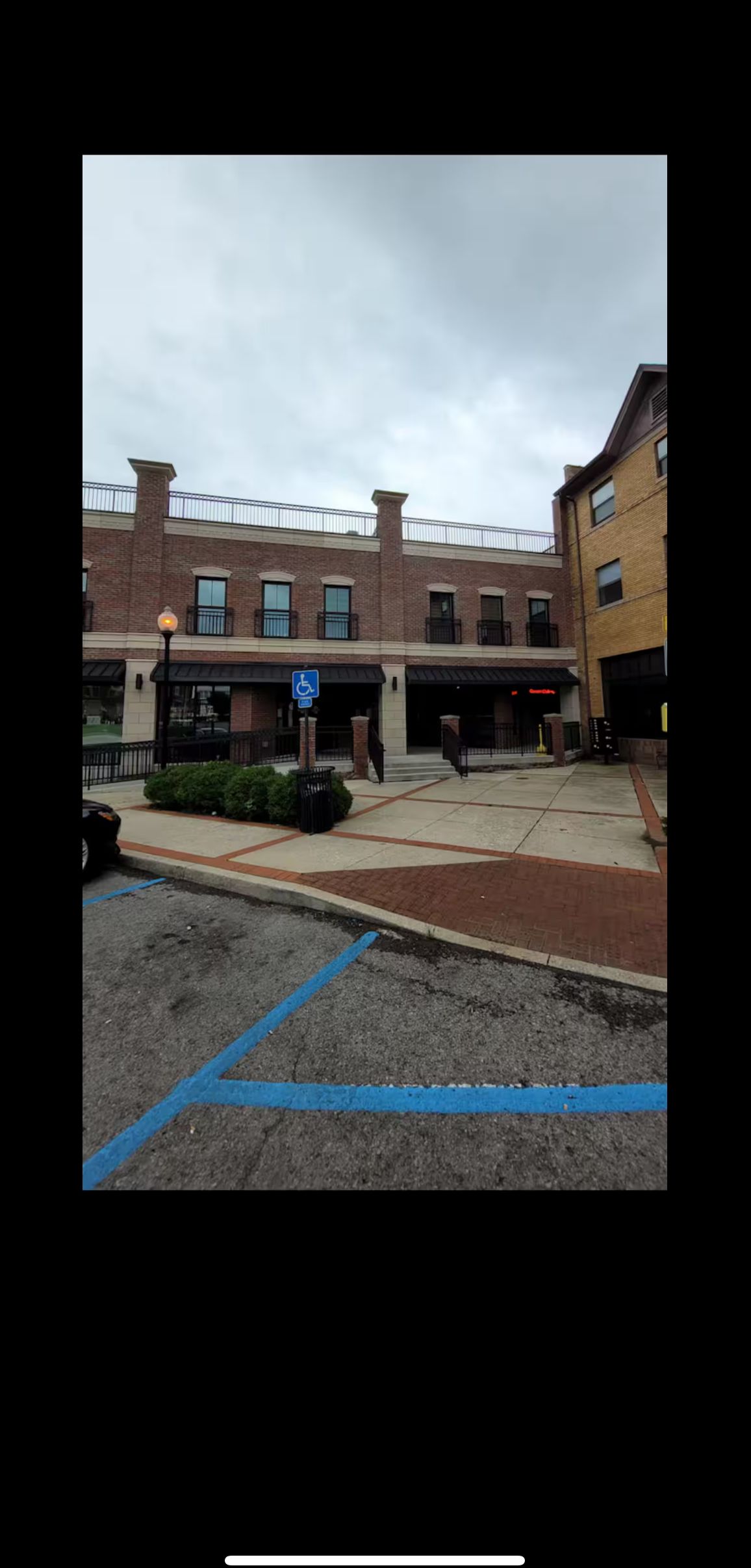 Un bâtiment avec une façade en briques, une entrée couverte et un panneau bleu indiquant une place de stationnement réservée aux personnes handicapées.