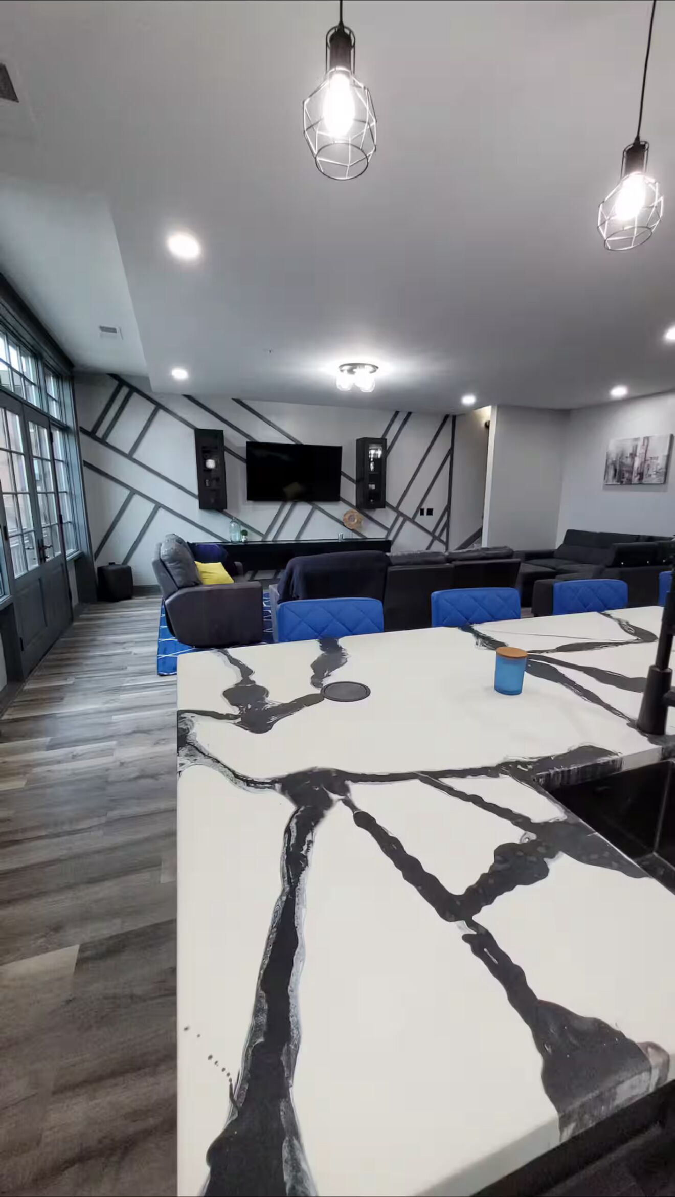 Un espace de détente moderne avec une grande table blanche, des sièges bleus et gris et des luminaires suspendus.