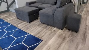 A modern living room with a sectional sofa, a blue geometric rug, and a cityscape painting on the wall.