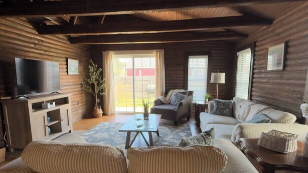 A log cabin interior with a sofa, armchairs, a coffee table, a TV, and a potted plant. - Lakeside Log Cabin Retreat- Close to Beach + Fishing + Boat Parking (Corpus Christi)