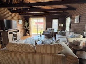 A log cabin interior with a sofa, armchairs, a coffee table, a TV, and a potted plant.