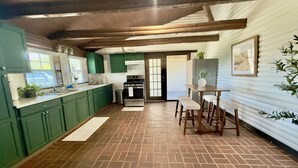 A kitchen with green cabinets, a brick floor, a dining area with wooden stools, and a ceiling with exposed beams. - Lakeside Log Cabin Retreat- Close to Beach + Fishing + Boat Parking (Corpus Christi)