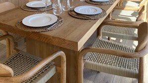 Un coin repas avec une longue table en bois, dressée pour six personnes, entourée de chaises en osier.