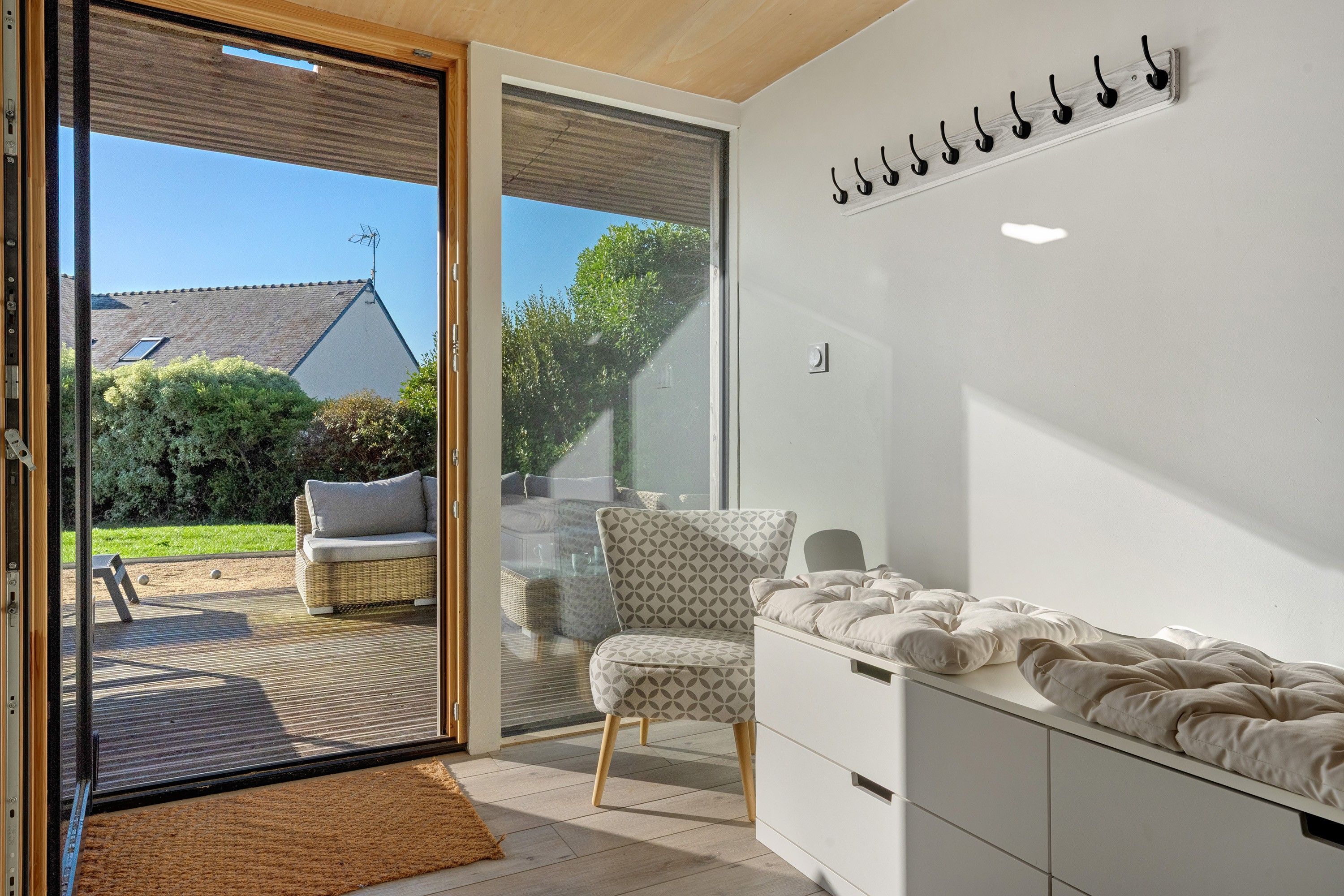 Een modern interieur met een schuifdeur naar een terras, een witte muur met kapstok en een bed met witte dekbed.