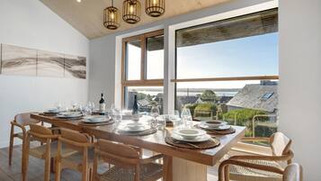 A dining area with a long wooden table set for six, large windows, and a view of the cityscape.