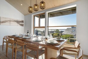 A dining area with a long wooden table set for six, large windows, and a view of the cityscape. - Villa Grande Est, Private Spa, Ideal for Family Holidays (Plouneour-Trez)