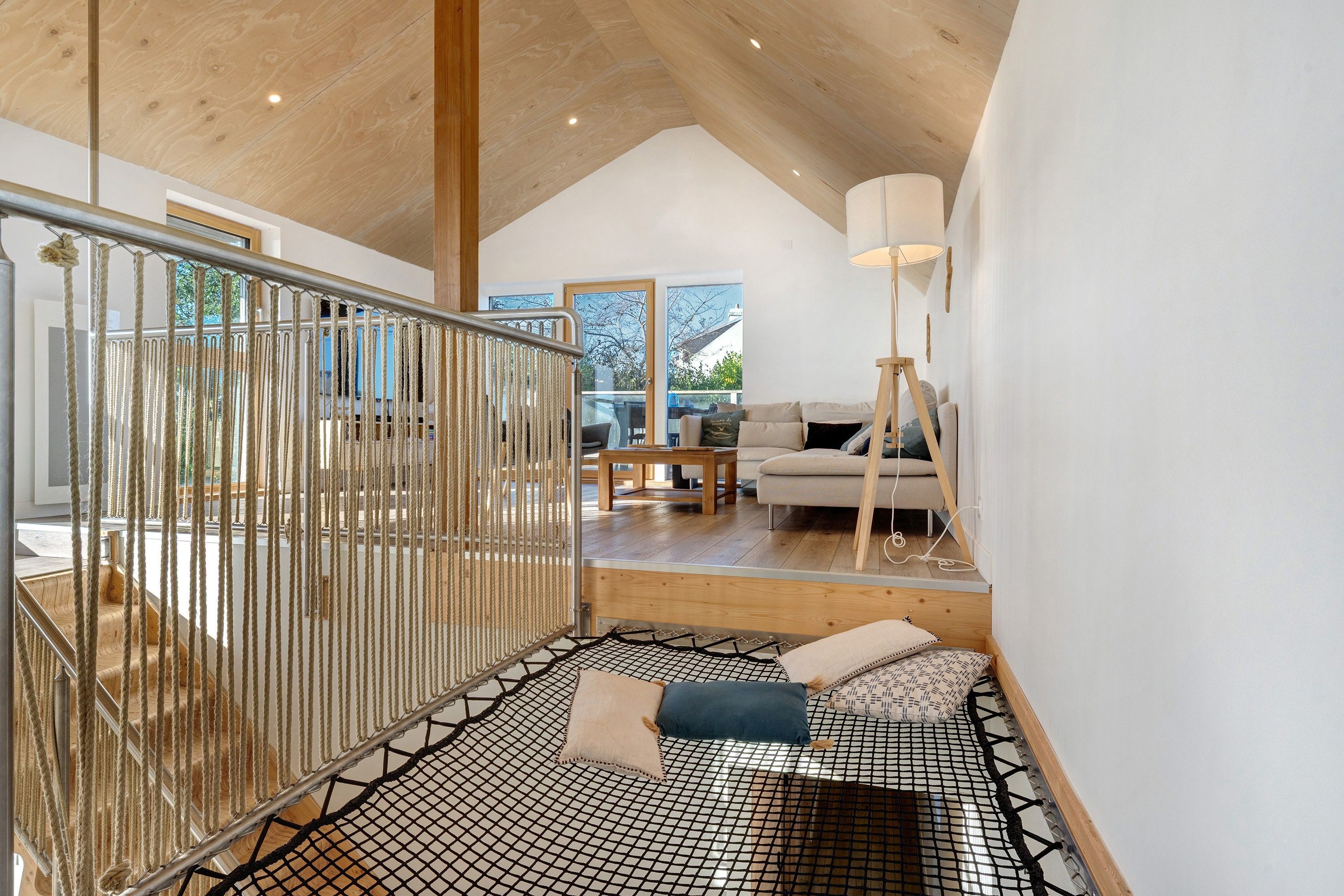Ein modernes Interieur mit einer Holztreppe, einer Sitzecke mit Kissen und Blick ins Freie.