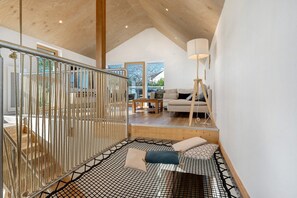 A modern interior with a wooden staircase, a seating area with cushions, and a view of the outdoors.