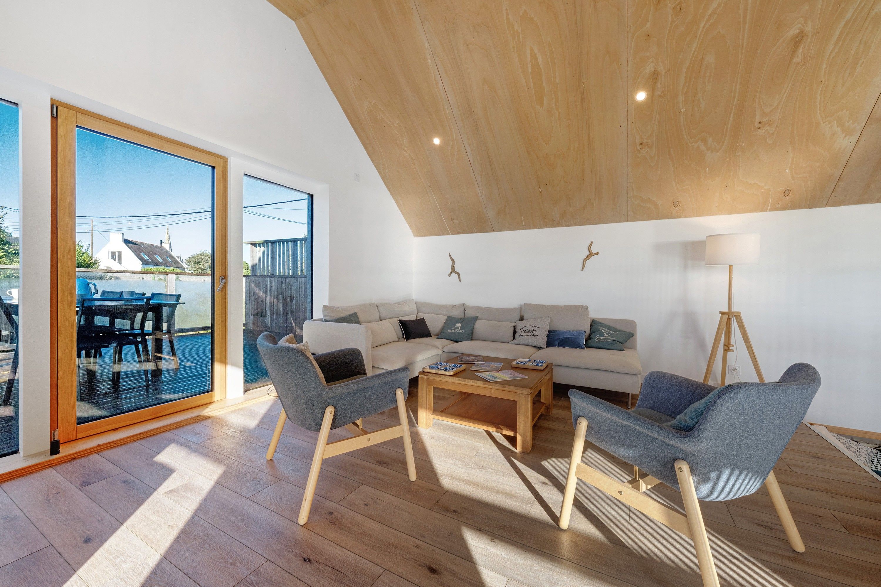 A modern living room with a wooden ceiling, a sectional sofa, two armchairs, a coffee table, and a floor lamp.