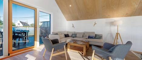 A modern living room with a wooden ceiling, a sectional sofa, two armchairs, a coffee table, and a floor lamp.