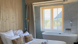 Une chambre à coucher avec un grand lit, une baignoire et une fenêtre avec des stores.