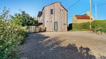 A wooden barn with a gravel driveway leading to a wooden gate.