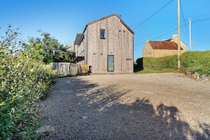 A wooden barn with a gravel driveway leading to a wooden gate.
