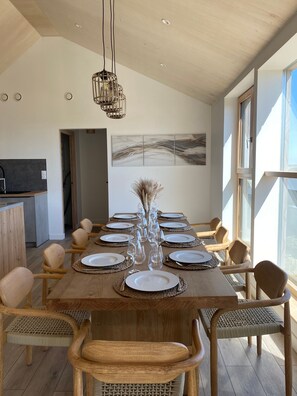 A dining area with a long wooden table set for a meal, surrounded by wicker chairs, with a modern pendant light above.