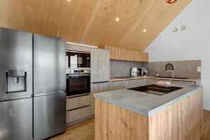 A modern kitchen with a stainless steel refrigerator, built-in oven, and a central island with a sink. - Villa Grande Est, Private Spa, Ideal for Family Holidays (Plouneour-Trez)
