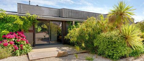 Een modern huis met een houten terras, een glazen entree en een tuin met diverse beplanting.