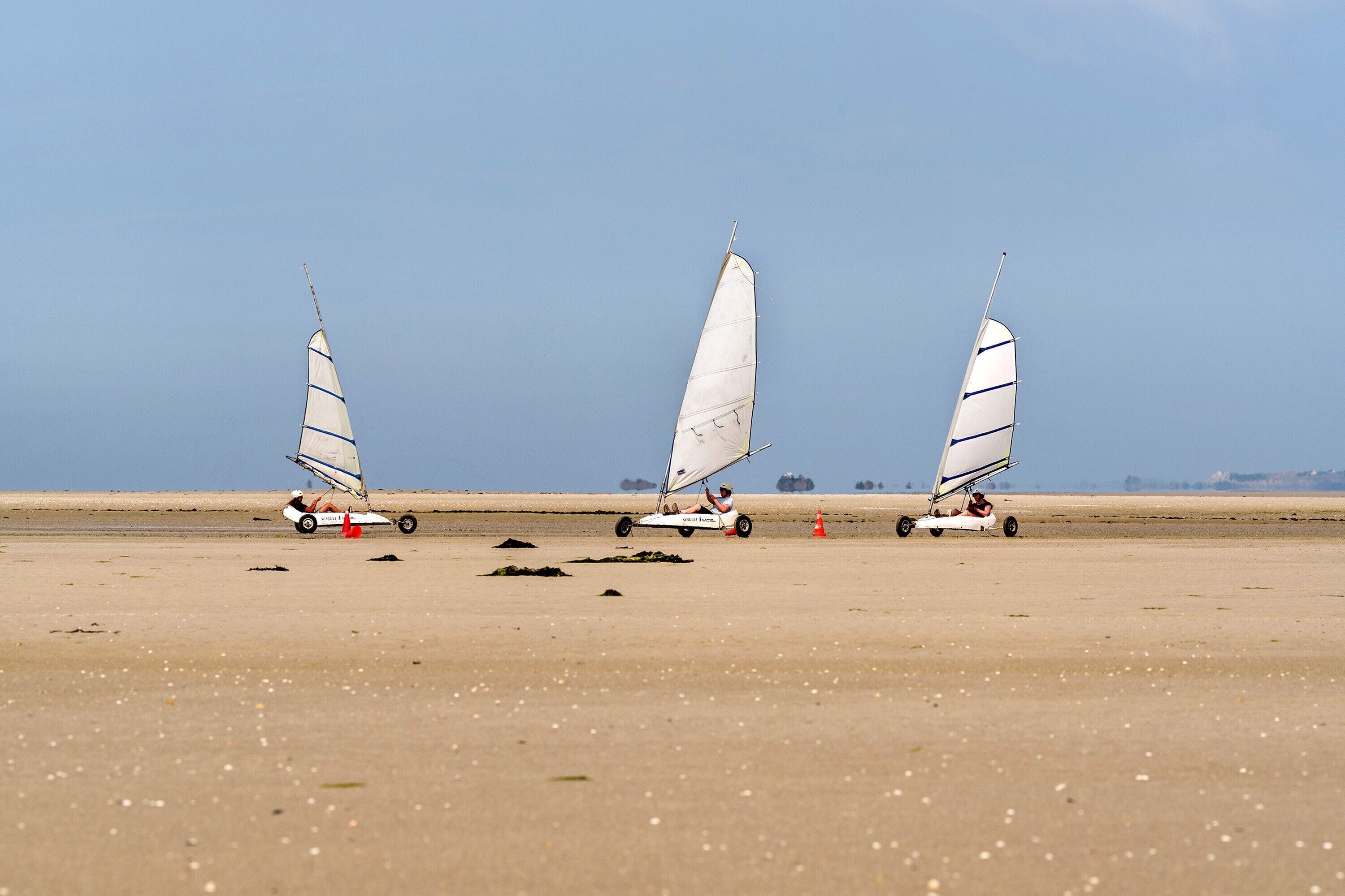 Three sailboats on a sandy beach with a clear sky.