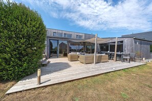 Ein moderner Außenbereich mit Korbmöbeln, einer Holzterrasse und einem großen Baum.