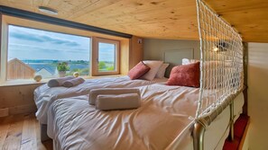 A bedroom with a large window, a bed with white linens, and a view of the landscape.
