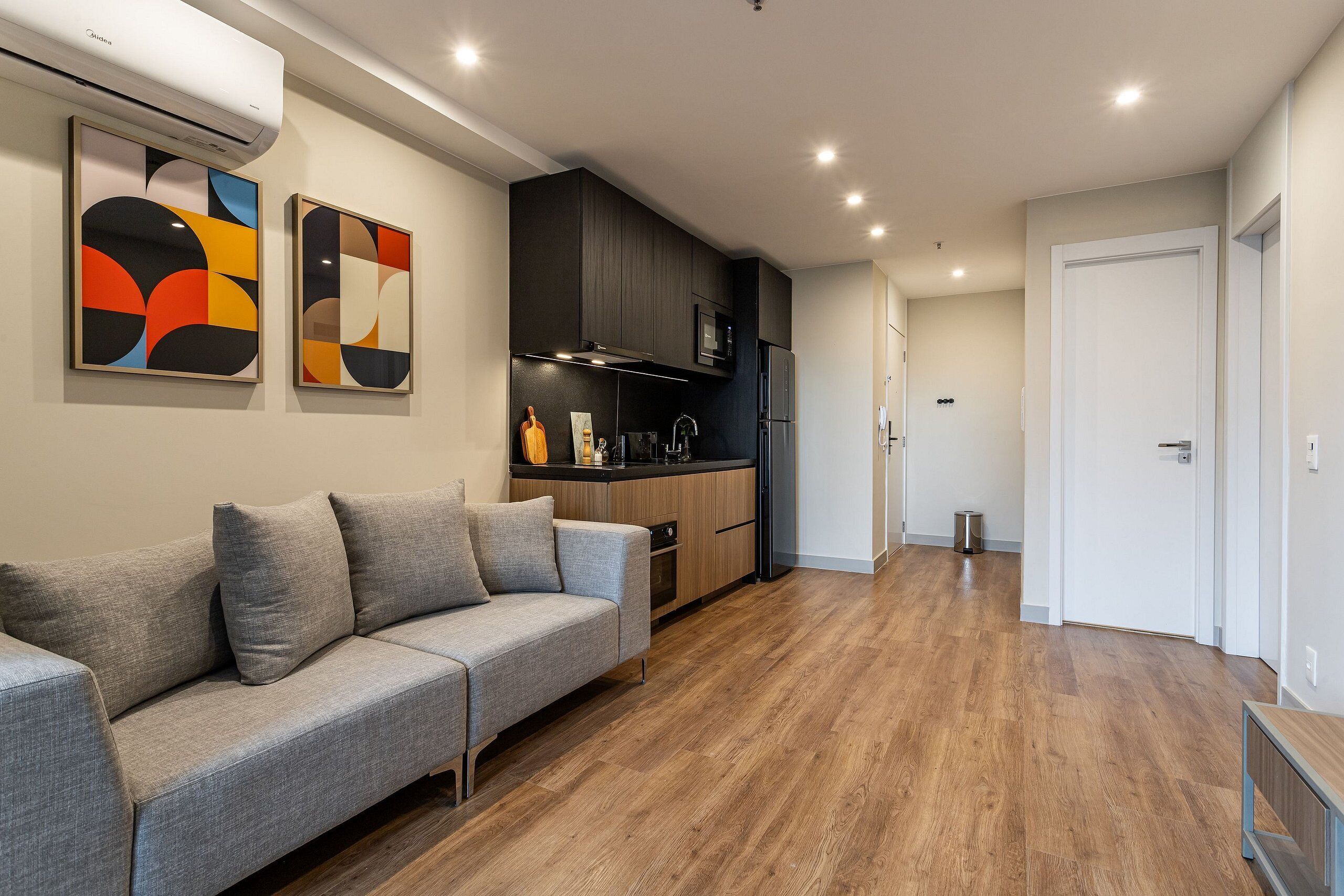 A modern kitchen with dark cabinets, a grey sofa, and abstract wall art.