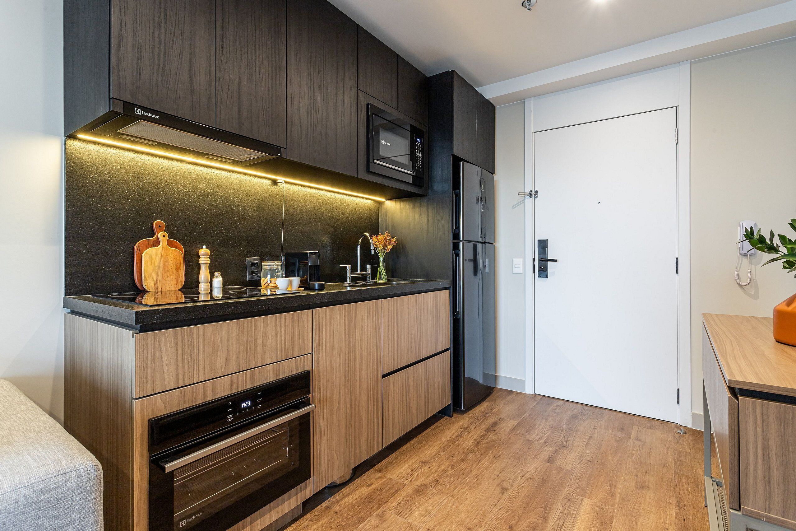 A modern kitchen with dark wood cabinets, a built-in microwave, and a stainless steel refrigerator.
