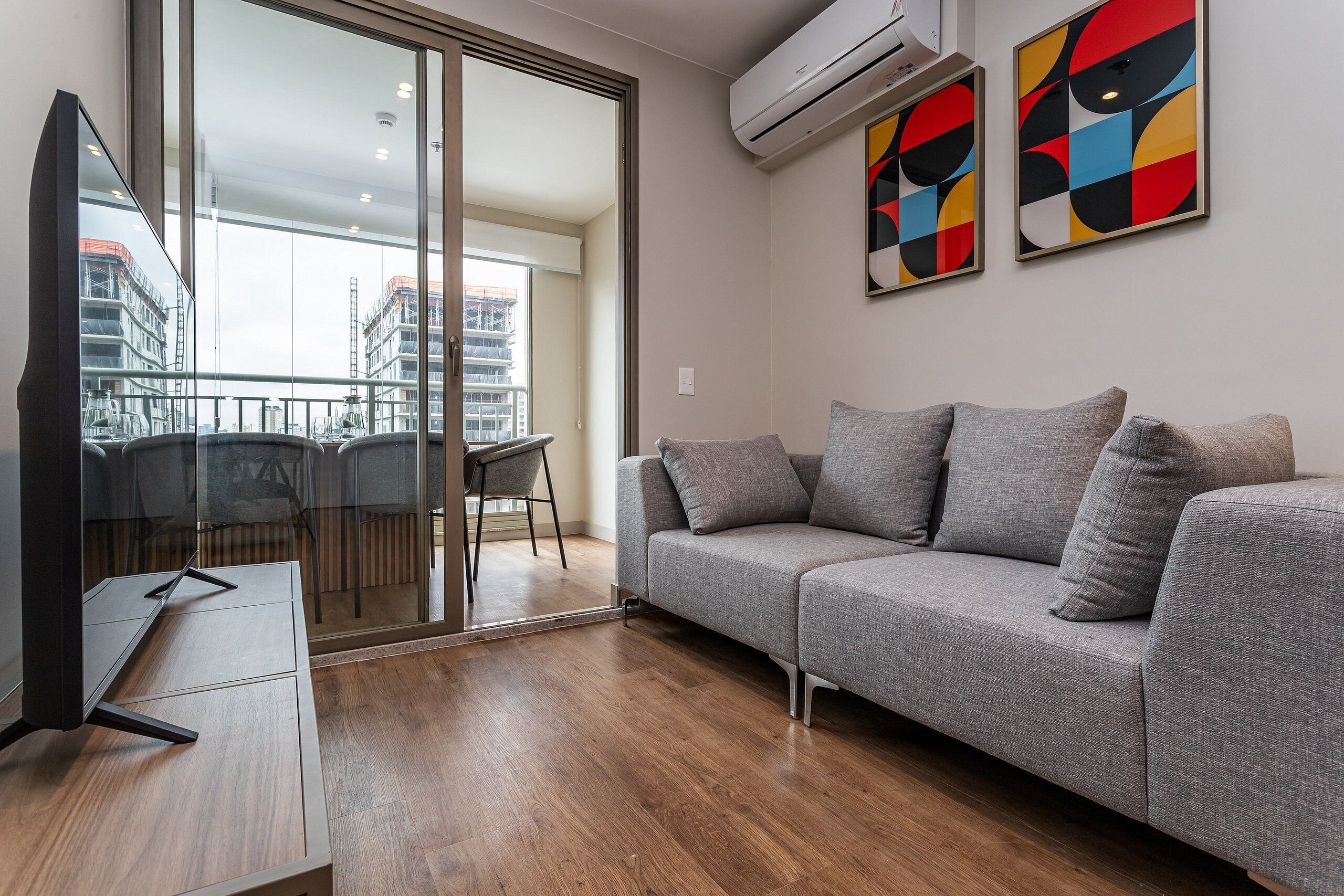 A modern living room with a grey sofa, a flat-screen TV, and a balcony with a glass door.
