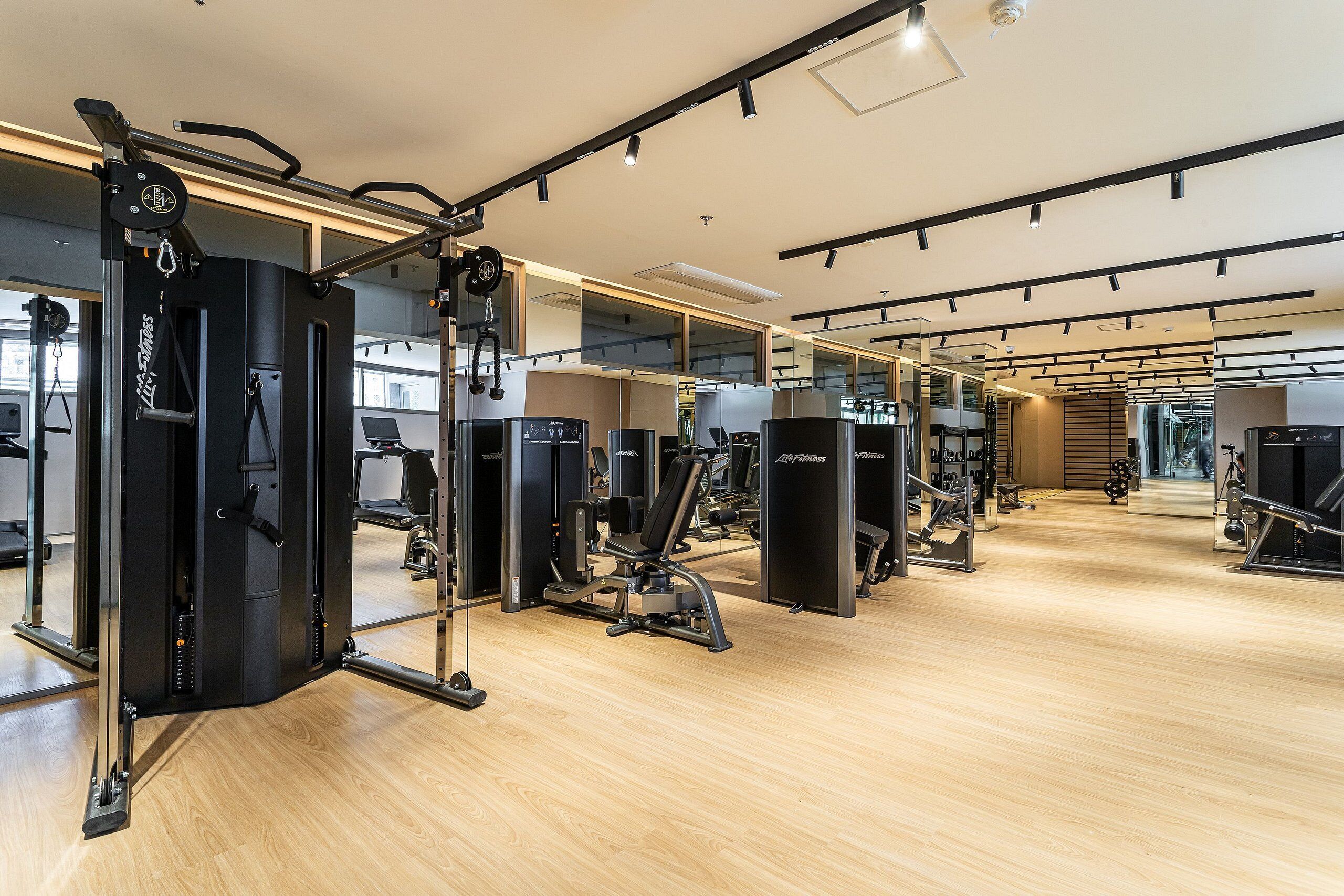 A modern gym with various exercise machines, wooden flooring, and large mirrors.