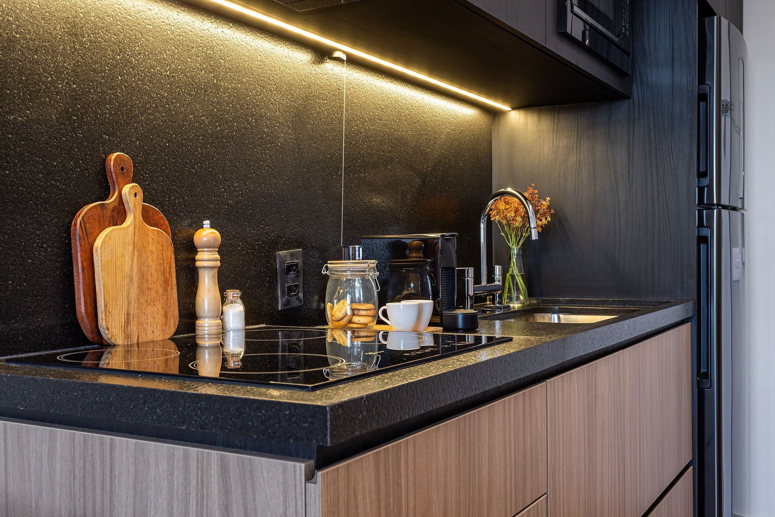 A modern kitchen with a black countertop, wooden cabinets, a coffee maker, and a vase with flowers.