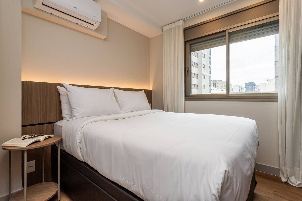A hotel room with a bed, bedside table, and a window with curtains.