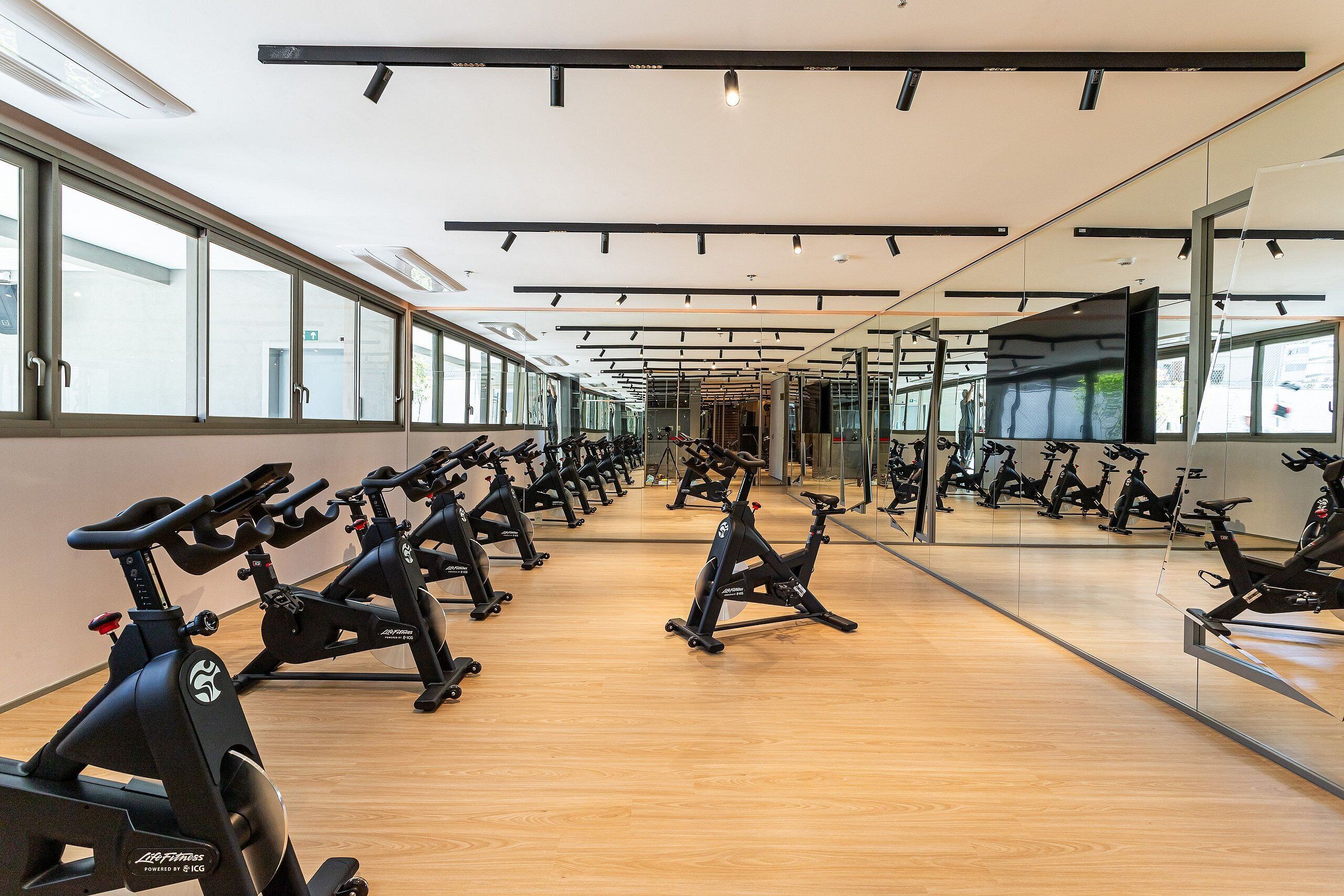 Ein Fitnessraum mit mehreren Fahrrädern, Holzböden und großen Fenstern.