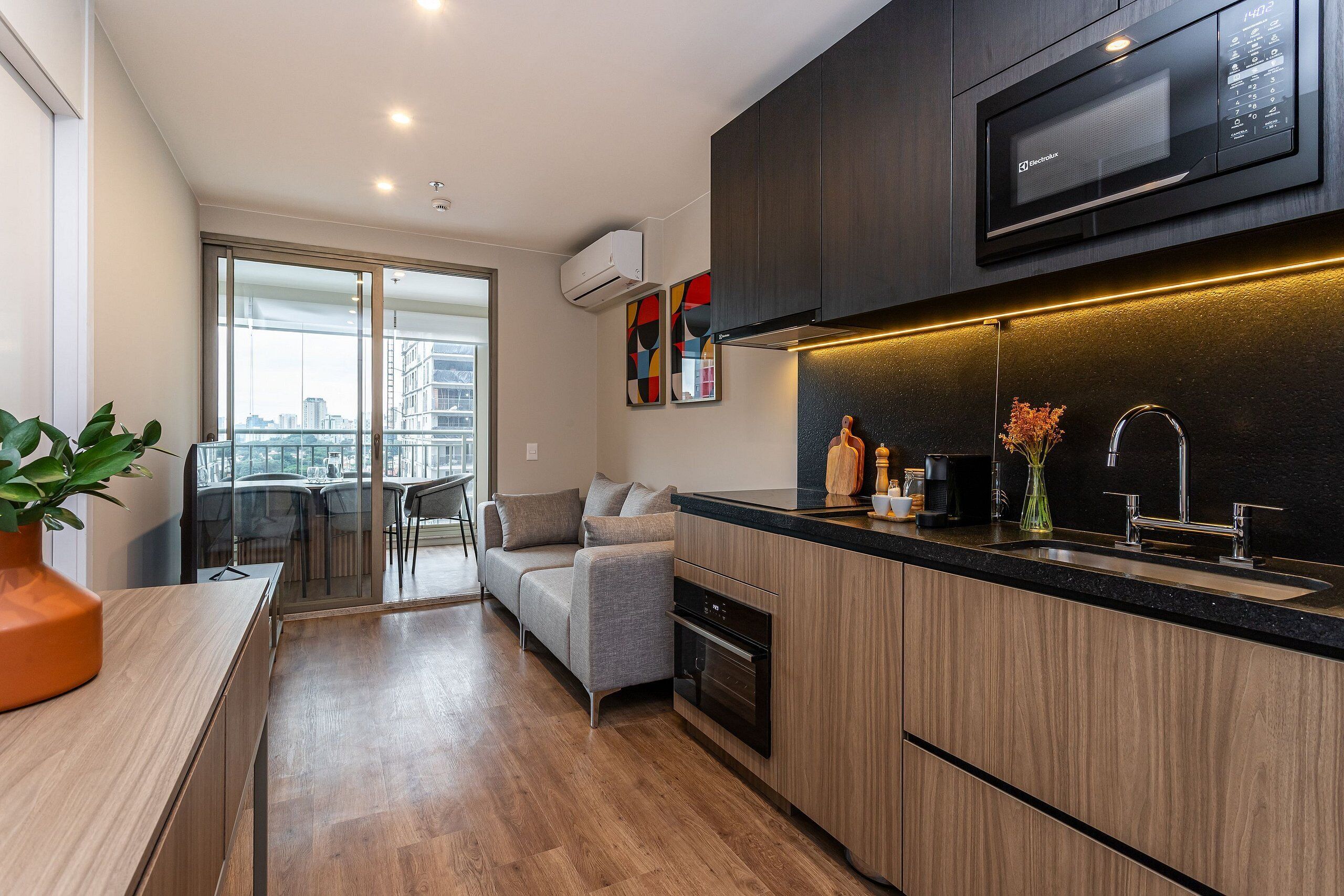 A modern kitchen with a built-in microwave, oven, and sink. There is a dining area with a sofa and a view of the city.