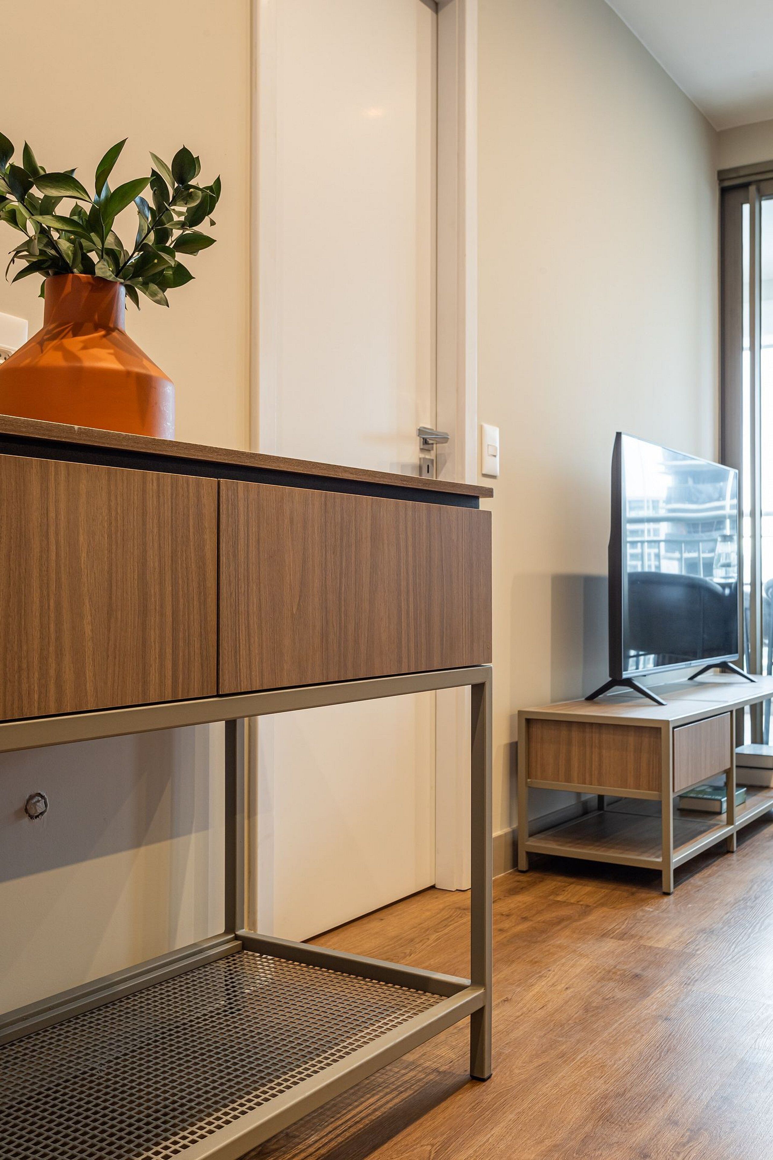 A modern room with a wooden console table, a potted plant, a television on a stand, and a large window.