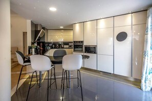 A modern kitchen with built-in appliances, a dining area with chairs, and a staircase leading to another level.