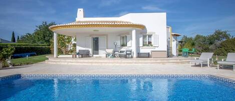 A poolside area with a covered seating area, a pool, and a white building with shutters.