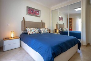 Une chambre à coucher avec un lit, une table de chevet, une lampe, un miroir et un tableau accroché au mur.