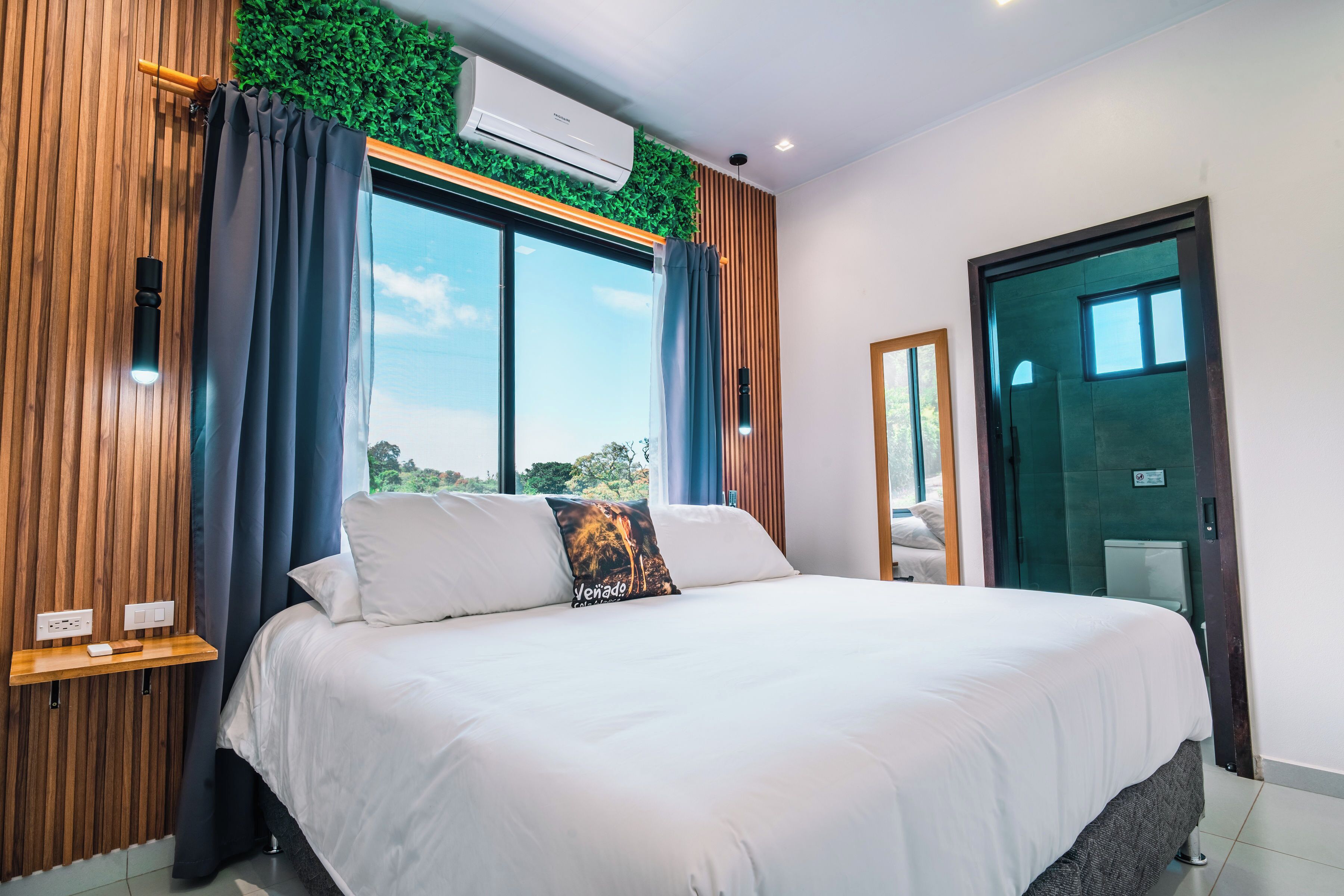 Habitación de hotel moderna con una cama grande, una ventana con cortinas, un equipo de aire acondicionado y un panel de pared de madera.