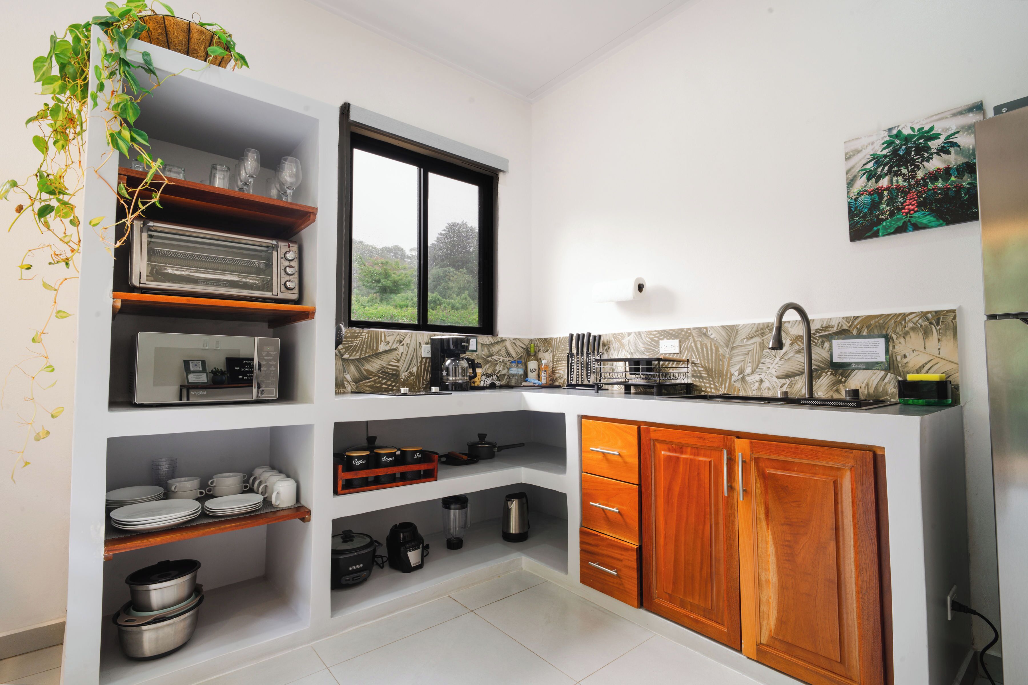 A compact kitchen with a built-in oven, a coffee machine, and a window providing a view of greenery.