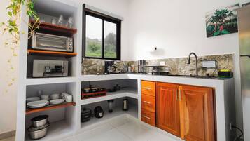 A compact kitchen with a built-in oven, a coffee machine, and a window providing a view of greenery.