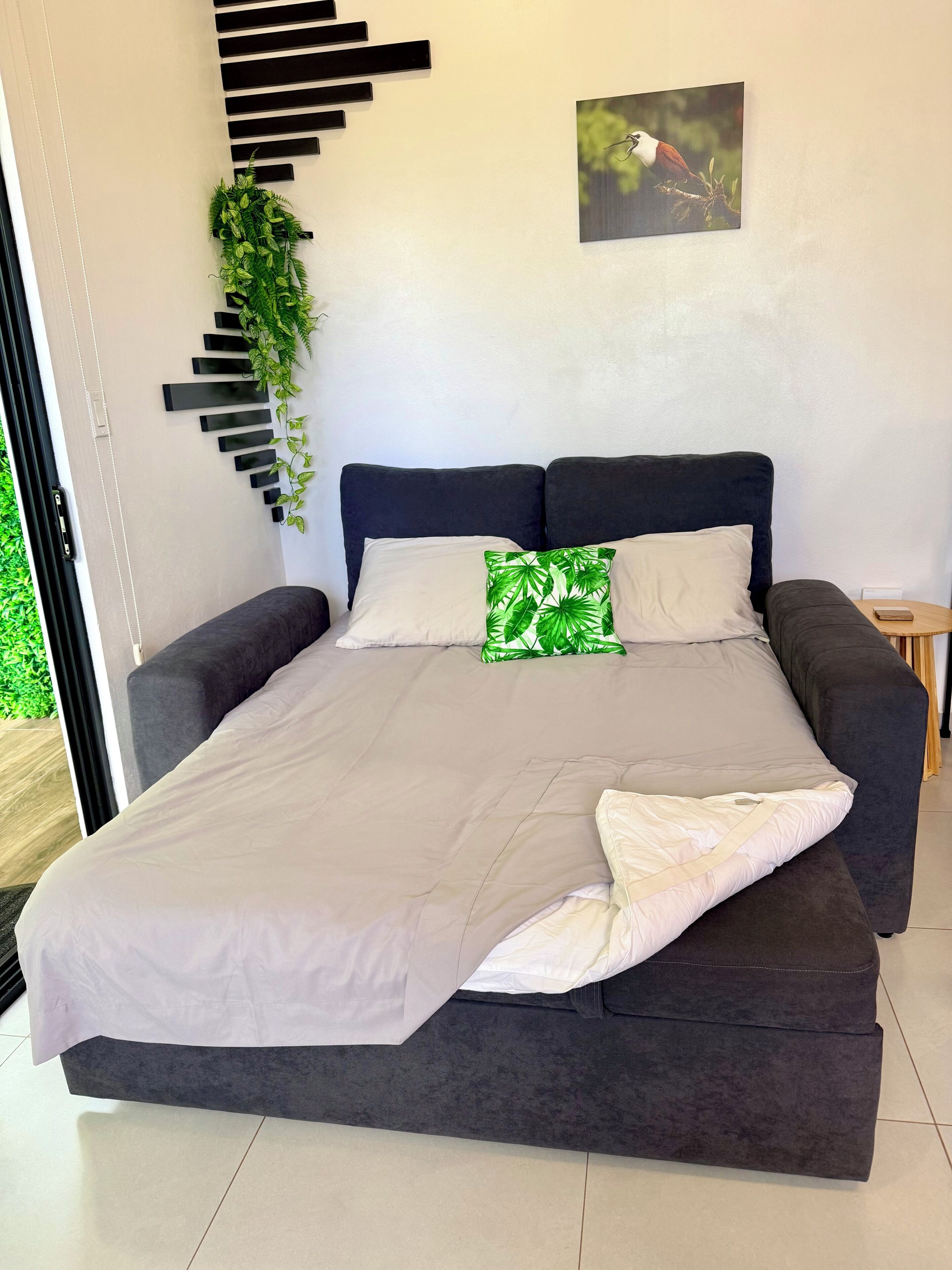 Een moderne slaapkamer met een bed, twee kussens, een hangende plant en een schilderij.