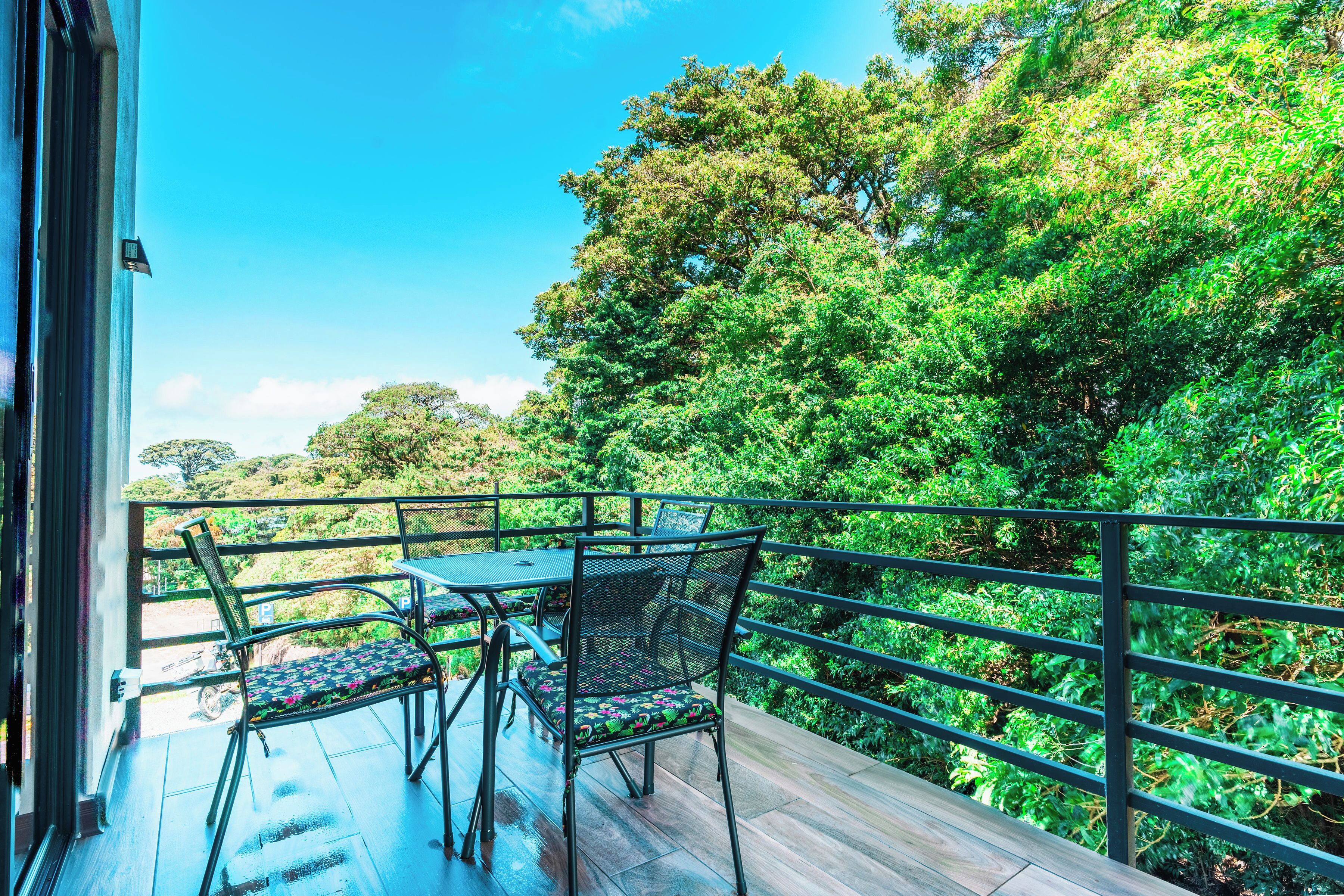 A balcony with a table and chairs, overlooking a lush green landscape.
