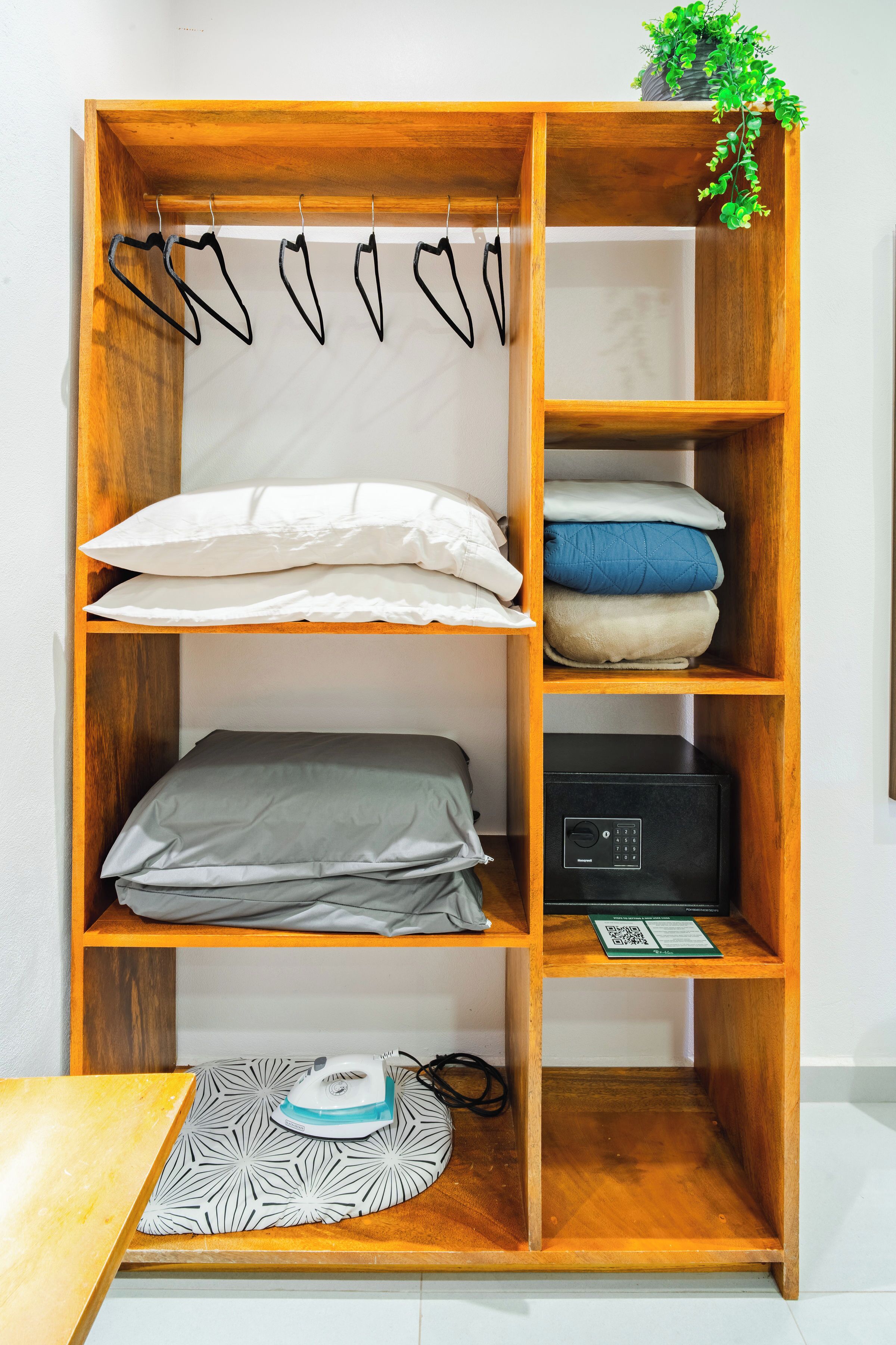 Une armoire en bois avec plusieurs étagères, une tringle à vêtements avec des cintres en forme de cœur, et une petite plante posée sur le dessus.