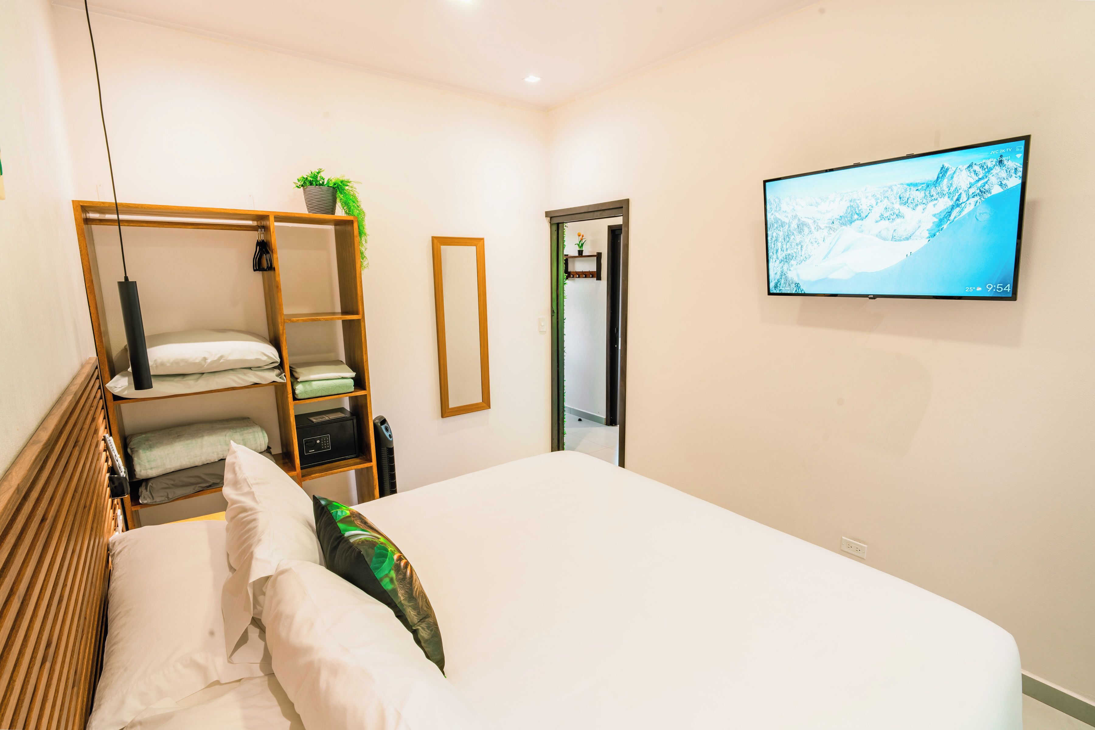 Un dormitorio con cama, armario, espejo, televisor y puerta.