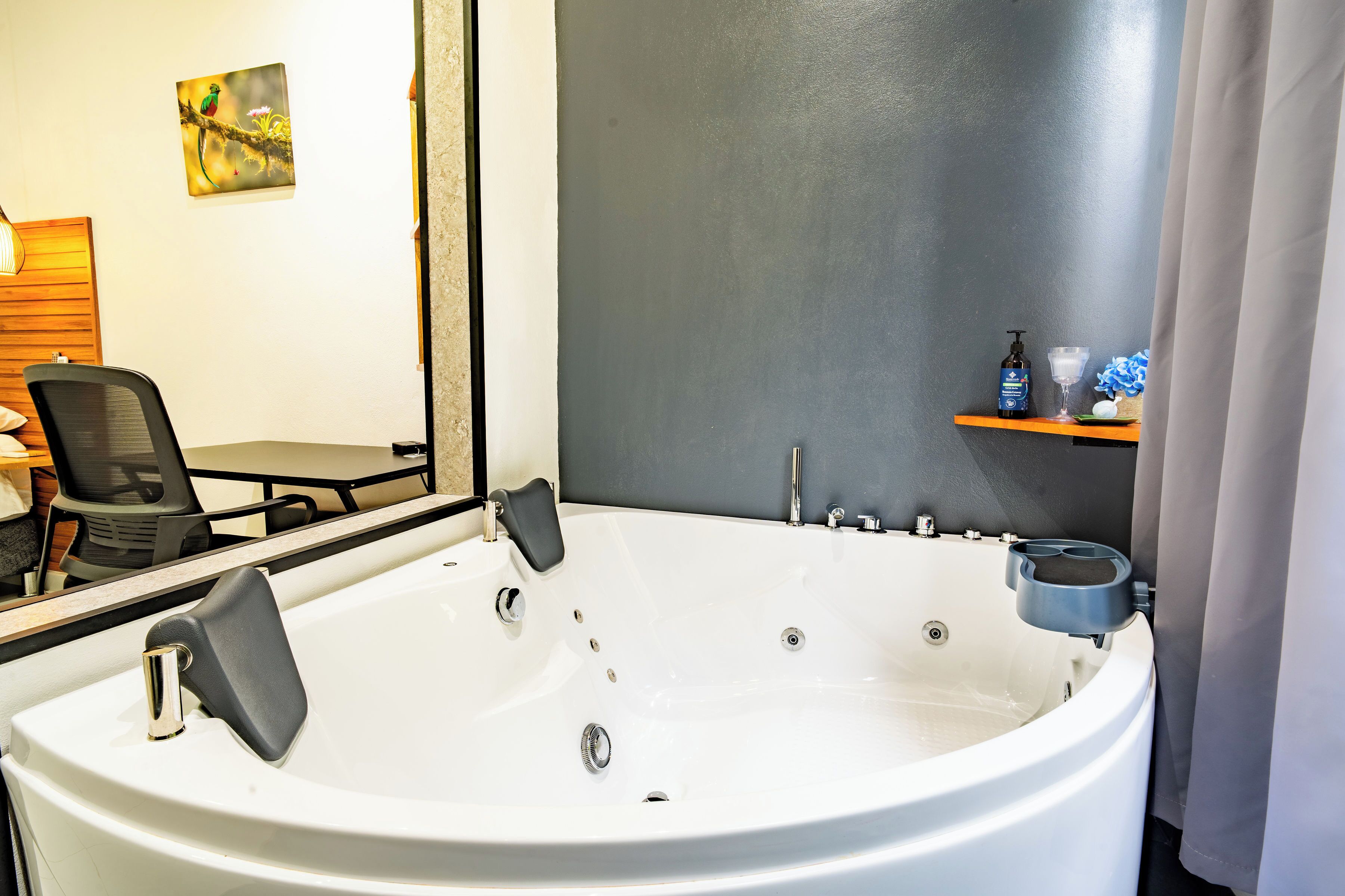 Ein modernes Badezimmer mit einer großen weißen Badewanne, einem Spiegel, einer kleinen Ablage mit Pflegeprodukten und einem hölzernen Stuhl.