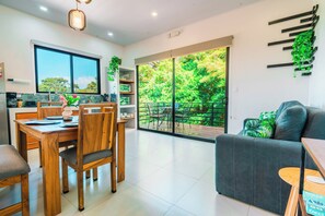 A modern kitchen with a dining area, a sofa, and a view of a lush garden through large sliding doors. - Biofilia Monteverde (Monteverde)