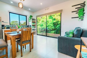 Una cocina moderna con comedor, sofá y vista a un jardín exuberante a través de amplios ventanales correderos.