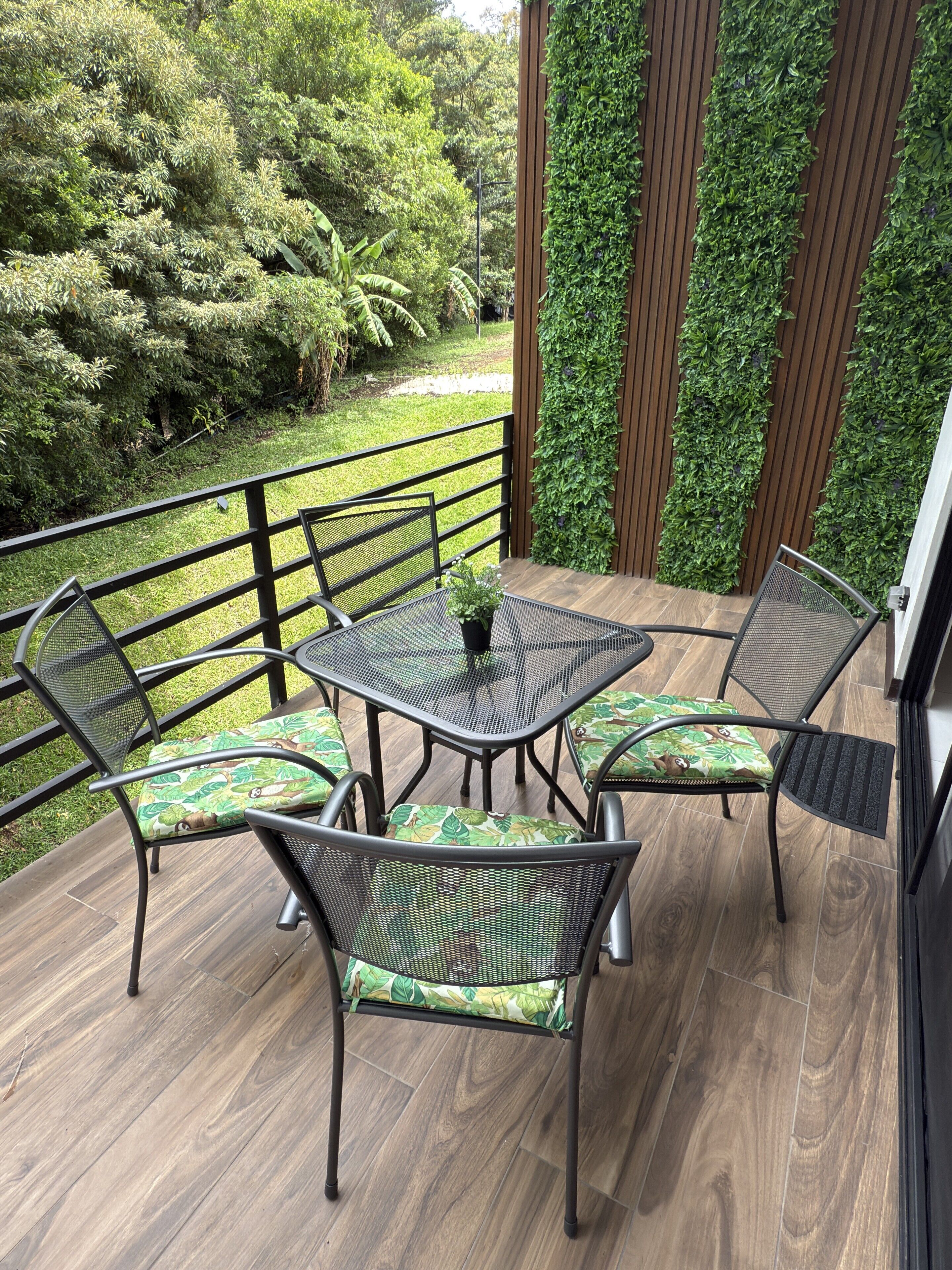 A covered patio with a table and chairs, surrounded by a wooden deck and a green wall.