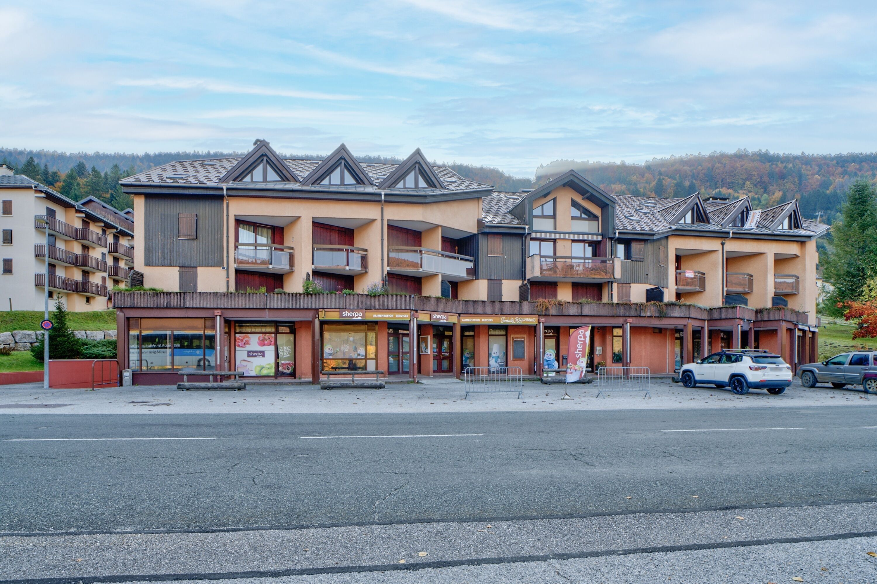 Un hotel de varios pisos con balcones, un estacionamiento y vistas del paisaje circundante.