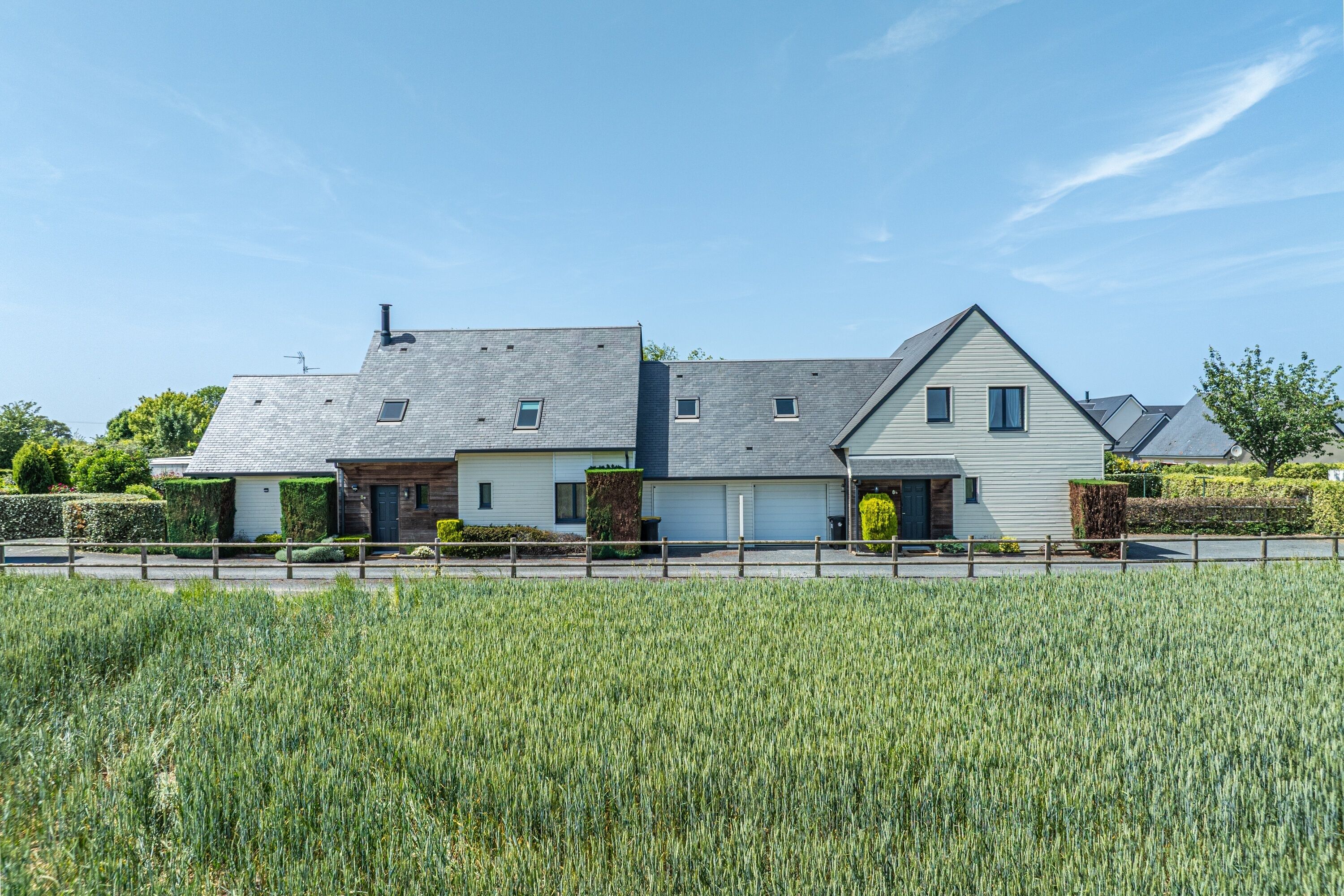 Une maison à deux étages avec un garage, entourée d’un champ.